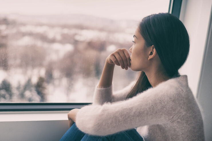 woman with relationship issues affecting her mental health comtemplative looking out the window alone.